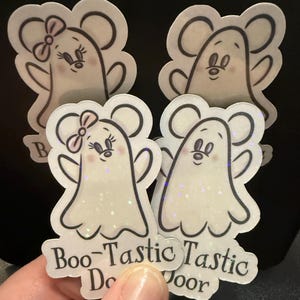May include: A collection of four stickers featuring cartoon ghost characters with mouse ears. Two ghosts have pink bows. The stickers have the text "Boo-Tastic Door". The ghosts are white with black outlines and glitter accents.