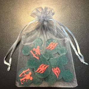 May include: A collection of green, glittery, round tokens with red designs and text, contained within a sheer, light blue drawstring bag. The tokens feature Mickey Mouse-inspired imagery and the word "LOVE".