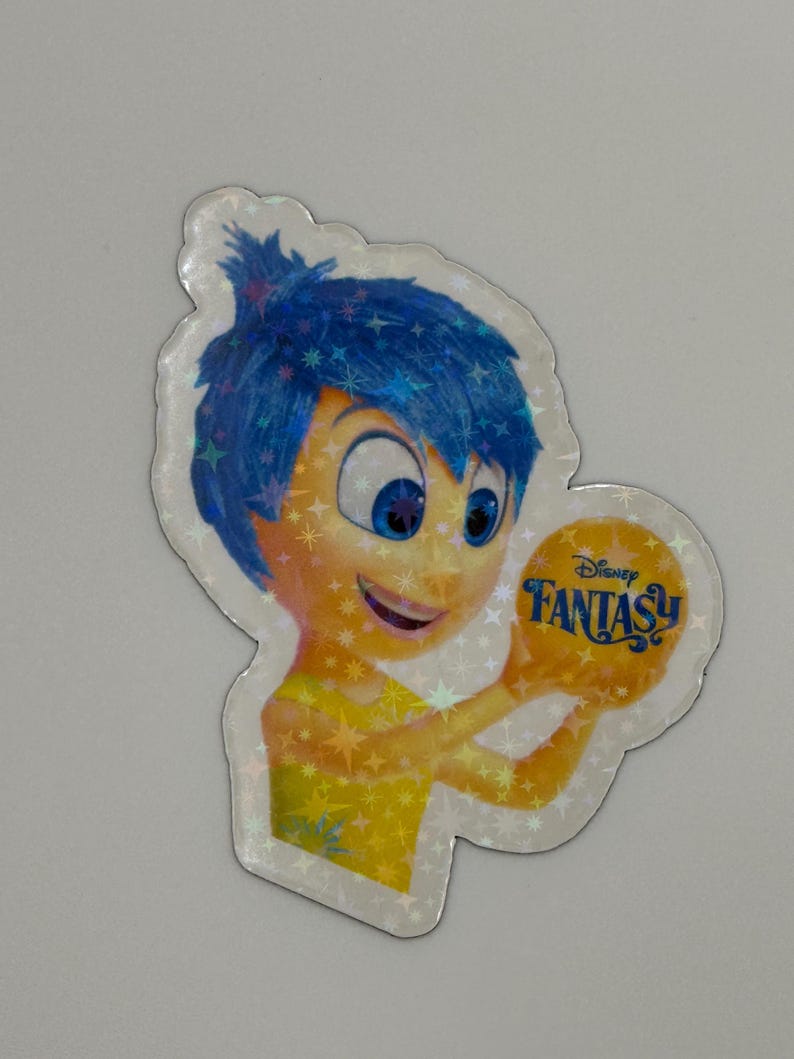 May include: A holographic sticker featuring the character Joy from the Disney movie Inside Out. Joy has blue hair and a yellow dress, holding a golden orb with the words "Disney Fantasy" on it. The sticker has a sparkly, iridescent finish.