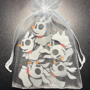 May include: A sheer white organza drawstring bag containing multiple flat, white ghost-like dog figures. Each figure features a round orange nose, a red collar, and large dark eye sockets, resembling the character Zero from The Nightmare Before Christmas.