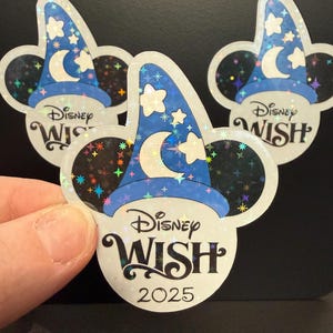 May include: Three stickers featuring a blue wizard hat with stars and a crescent moon, set against a black background. The stickers have the text "Disney WISH 2025" in a stylized font, with the iconic Mickey Mouse ears shape.