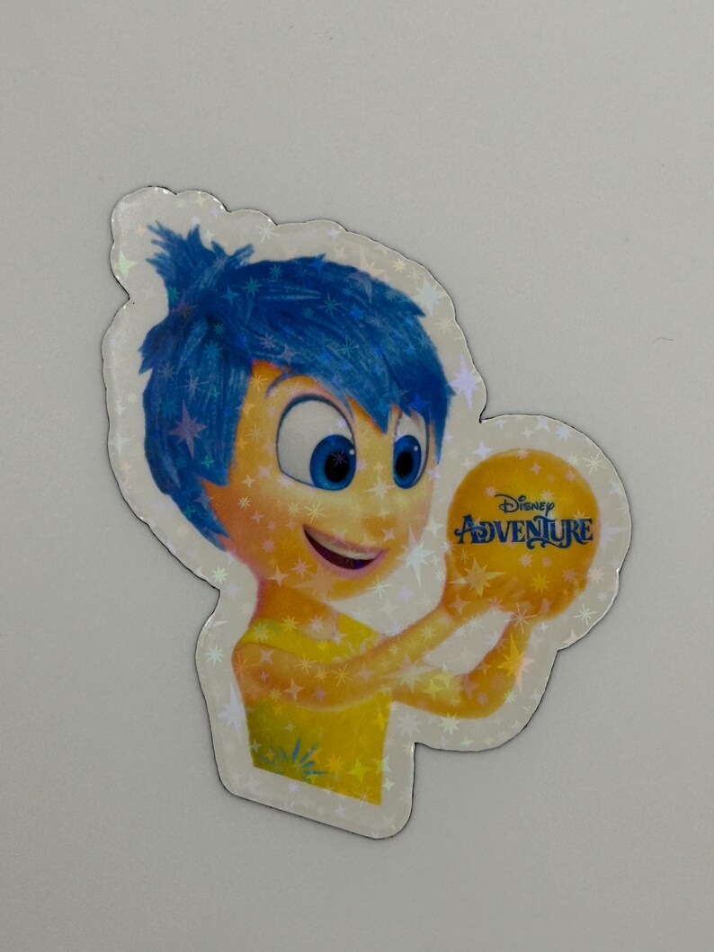 May include: A holographic sticker featuring the character Joy from the Disney movie Inside Out. Joy has blue hair and a yellow dress, holding a yellow ball with the text "Disney Adventure". The sticker has a star-shaped border.