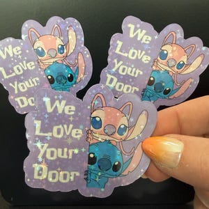May include: Holographic stickers featuring the characters Angel and Stitch from Lilo & Stitch. The stickers are purple with the text "We Love Your Door". Angel is pink, and Stitch is blue. The stickers are in a cloud shape.
