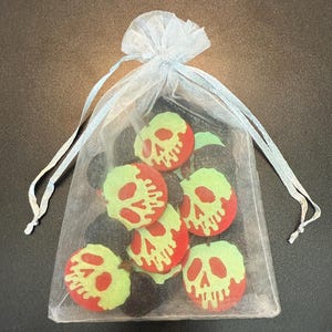 May include: A sheer, light blue drawstring bag filled with several round, red and green skull-shaped embellishments. The bag is tied with a light blue ribbon. The skulls have a green face and red outline.