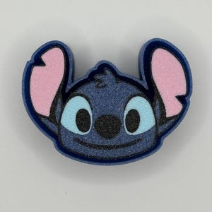 May include: A blue character face with pink ears and light blue eyes. The character has a black nose and a smiling mouth. The outline of the face is dark blue. The image is a close-up of the character's face.