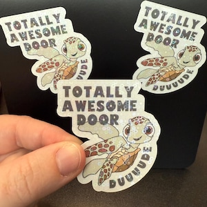 May include: Three stickers with a cartoon sea turtle design. The stickers have the text "TOTALLY AWESOME DOOR" and "DUUUUDE". The turtle is light green, brown, and tan with a smiling face.