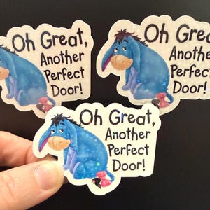May include: Three stickers featuring Eeyore from Winnie the Pooh. Each sticker shows Eeyore in a seated position with the text "Oh Great, Another Perfect Door!" in black font. The stickers have a white border.