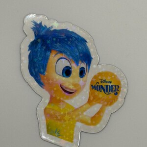 May include: A holographic sticker featuring the character Joy from the Disney movie "Inside Out." Joy has blue hair and a yellow outfit, holding a yellow orb with the word "Wonder" on it.