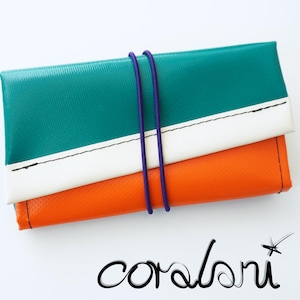 Könnte beinhalten: Eine rechteckige Geldbörse in Teal, Weiß und Orange, gesichert mit einem lila Gummiband. Die Geldbörse hat eine strukturierte Oberfläche und einen weißen Streifen. Das Wort "coralori" ist unten in Kursivschrift geschrieben.