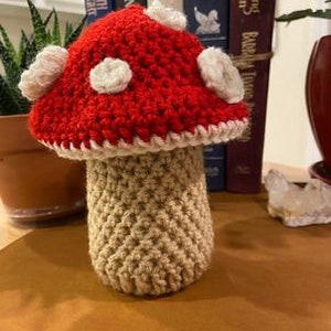 May include: A crocheted mushroom with a red cap and white spots, and a beige stem.