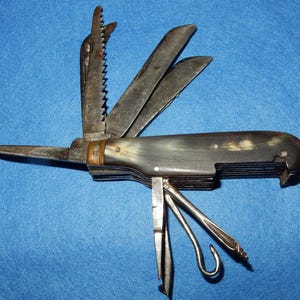 Puede incluir: Un cuchillo de bolsillo multiusos con mango de cuerno y múltiples hojas, incluyendo una sierra, un abridor de botellas y un gancho.