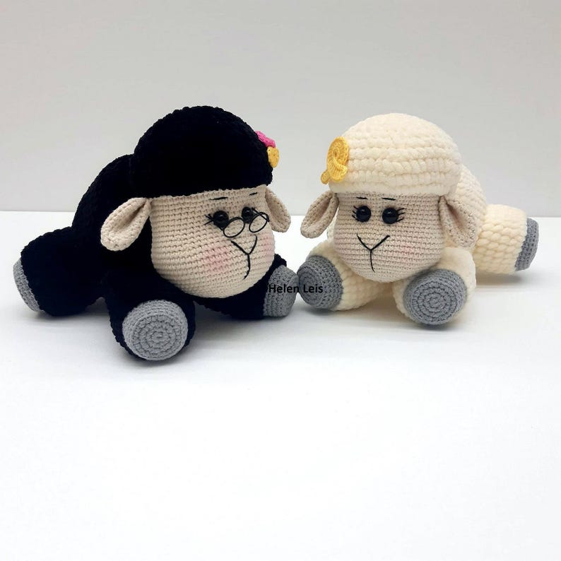 May include: Two crocheted sheep toys, one black with glasses and a pink flower, the other white with a yellow flower. Both have grey hooves.