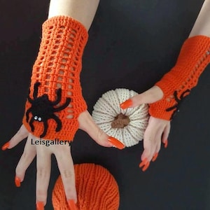 May include: Orange crochet fingerless gloves with a black spider applique. The gloves are open-weave and feature a decorative spider on the back of the hand. A white pumpkin and orange yarn ball are also in the image. Halloween theme.