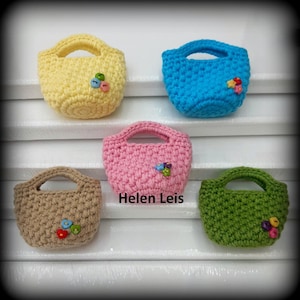 Può includere: Cinque mini borse all'uncinetto gialle, blu, rosa, marroni e verdi. Ogni borsa ha un manico ed è decorata con bottoni colorati. Il testo "Helen Leis" è visibile sulla borsa rosa.