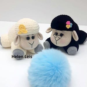May include: Two crocheted sheep plushies, one white with a yellow bow and one black with a flower and glasses. A blue fluffy ball sits in front of the sheep.