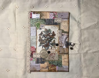 Op de afbeelding: Een rechthoekig dagboek met een collage-omslag met vintage vlinderillustraties, bloemmotieven, kanten randen en papieren ephemera. De omslag bevat een rond label met de tekst Field Specimen Label en een stempel met de tekst Aug 1.