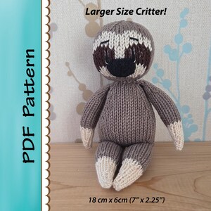 May include: A knitted sloth doll with a gray body, brown and white face, and white accents on the hands and feet. The doll is approximately 7 inches tall and 2.25 inches wide. Text on the image reads "Larger Size Critter!" and "PDF Pattern".