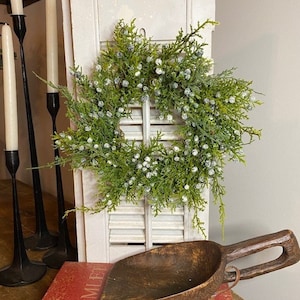 May include: A wooden scoop with a brown handle, sitting on a red book with the word "HAMLET" visible. A green wreath with white berries is in the background.