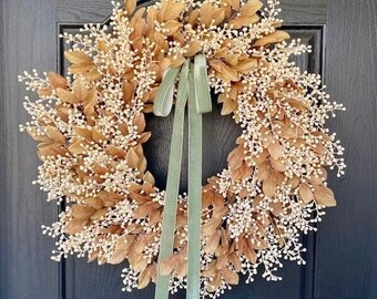 May include: A round wreath featuring brown leaves and white berry clusters. A sage green ribbon is tied in a bow and hangs down. The wreath is displayed on a black door.