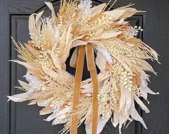 May include: A decorative wreath featuring dried flowers and foliage in shades of cream, beige, and brown. The wreath is adorned with a tan velvet ribbon. This wreath is perfect for adding a touch of natural elegance to any home decor.
