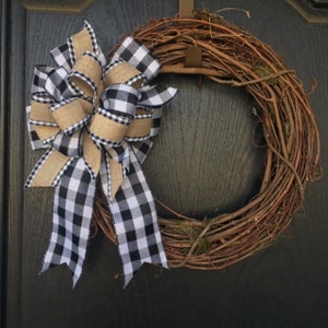 May include: A grapevine wreath with a black and white buffalo check ribbon bow and a burlap ribbon bow.