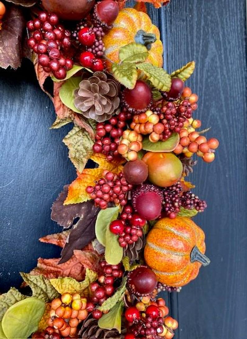 May include: A fall-themed wreath with pumpkins, berries, and leaves in shades of orange, red, and brown. The wreath includes pinecones and faux fruit, creating a festive autumn decoration.