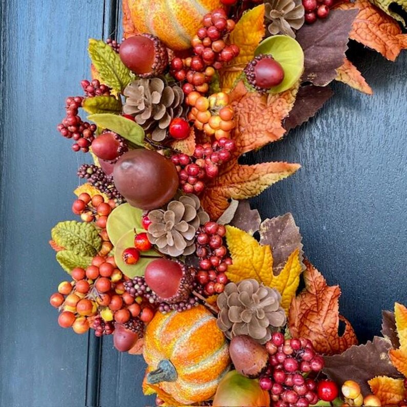 May include: A fall-themed wreath with pumpkins, pinecones, berries, and leaves in shades of orange, red, brown, and green. The wreath is a decorative item for the autumn season, suitable for a door or wall.