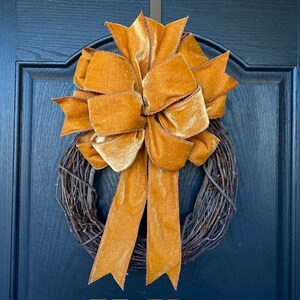 May include: A golden yellow velvet bow tied on a brown twig wreath. The wreath is hanging on a dark blue door.