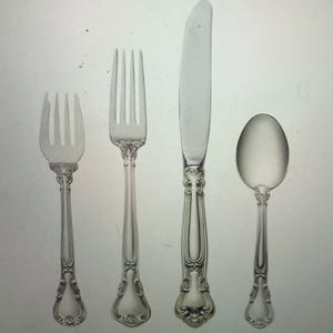 May include: A set of four silver-plated flatware pieces, including a knife, fork, and two spoons. The pieces have ornate handles with a floral design.