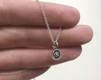 May include: A silver chain necklace with a small, round pendant featuring a black evil eye design.