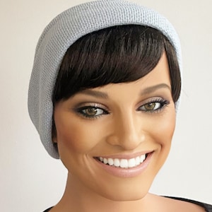 May include: A woman with short, dark brown hair is wearing a light blue knitted beanie. She is smiling and looking at the camera.