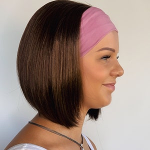 May include: A woman with shoulder-length brown hair wearing a pink headband. She is wearing a white vest top and a silver necklace.