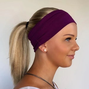 May include: A purple headband made of soft fabric. The headband is worn by a person with blonde hair pulled back in a ponytail.