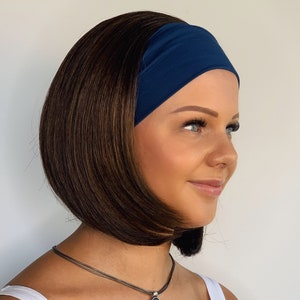 May include: A woman with brown hair wearing a navy blue headband and a silver necklace with a round pendant. She is wearing a white vest top.