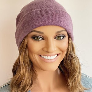 Può includere: Un berretto di lana viola fatto di tessuto a maglia morbido. Il berretto è largo e ha un design semplice.