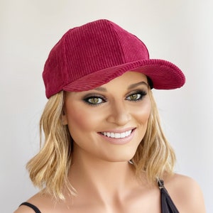May include: A burgundy corduroy baseball cap with a curved brim. The cap is made of a soft, textured fabric.