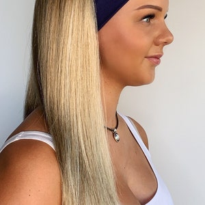 May include: A woman with long blonde hair wearing a navy blue headband. The woman is also wearing a white tank top and a silver pendant necklace. The hair is straight and falls down the woman's back.