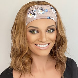 May include: A light brown wavy wig with a floral headband. The headband is a light brown colour with a white and blue floral pattern.