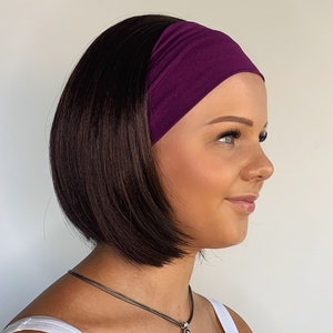 May include: A woman with dark brown hair is wearing a purple headband. She is wearing a white vest top and a silver necklace with a round pendant.