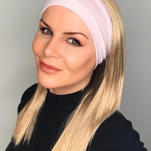May include: A woman with long, straight, blonde hair is wearing a pink headband. She is wearing a black turtleneck sweater.