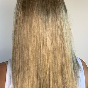 May include: A person's long, straight, blonde hair, viewed from the back. The hair is a mix of light and medium blonde shades, with a slight gradient effect. The person is wearing a white tank top.
