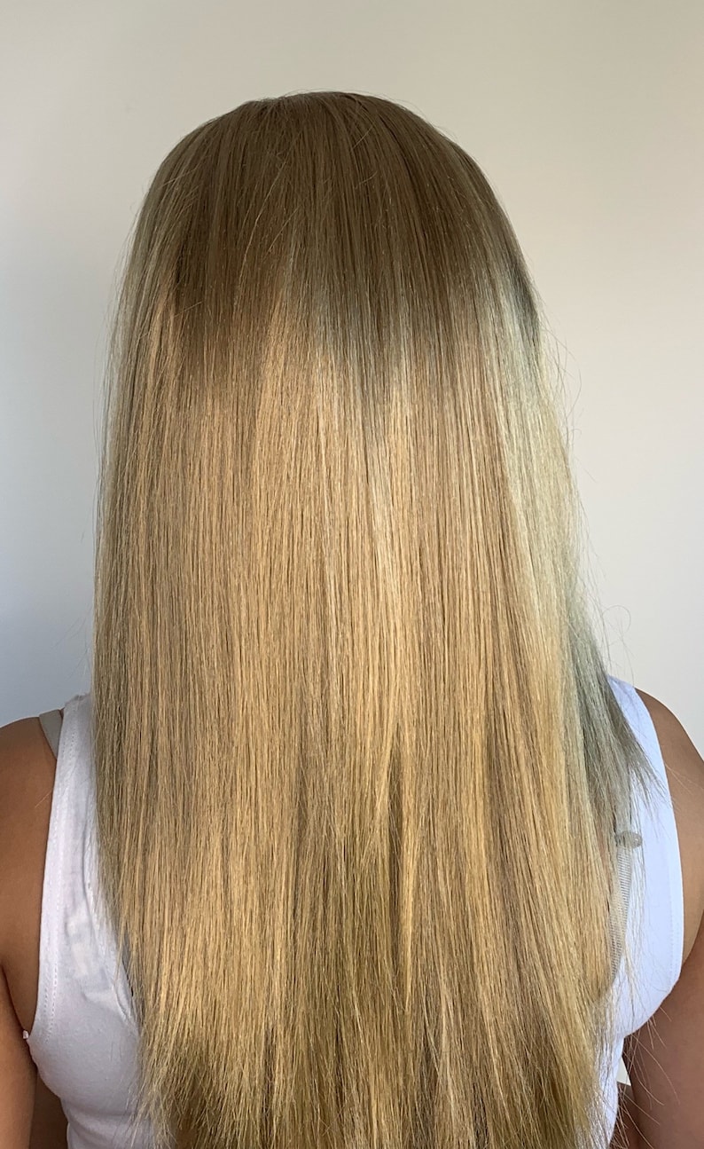 May include: A person's long, straight, blonde hair, viewed from the back. The hair is a mix of light and medium blonde shades, with a slight gradient effect. The person is wearing a white tank top.