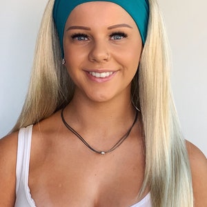 May include: A woman with long blonde hair is wearing a teal headband. She is wearing a white vest top and a silver necklace.