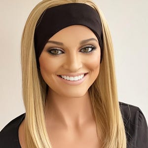 May include: A woman with long blonde hair wearing a black headband. The headband is made of a soft, stretchy material. The woman is smiling, and her eyes are open. She is wearing a black top.