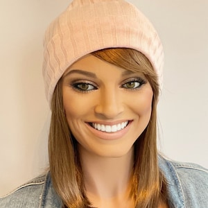 Puede incluir: Un gorro de punto de color rosa con textura de canalé. El gorro lo lleva puesto una persona con el pelo largo y castaño.