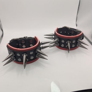 May include: Two black leather bracelets with silver studs and spikes. The bracelets have a red inner lining.