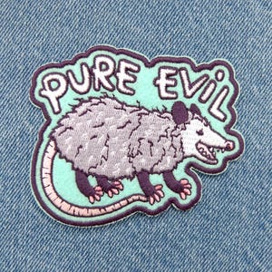 May include: An embroidered patch featuring a light gray opossum with dark purple limbs and a pink tail. The opossum is set against a light mint green background with a dark purple border. The text PURE EVIL is stitched in white above the opossum.