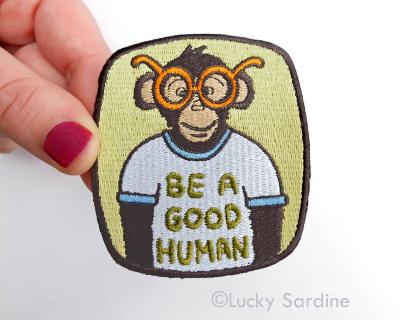 Pu&ograve; includere: Toppa ricamata termoadesiva con una scimmia dei cartoni animati che indossa occhiali rotondi arancioni e una maglietta bianca con il testo "Be a good human".