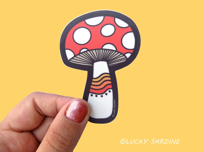 May include: A red and white mushroom sticker with a brown stem and orange and yellow stripes. The sticker has a black outline and the text "&copy; Lucky Sardine" at the bottom.