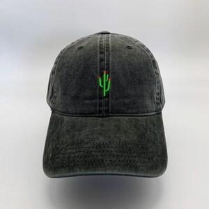 May include: A black denim baseball cap with a green cactus embroidered on the front. The cactus has red flowers on top.